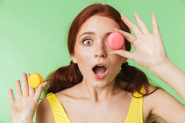 Ragazza rossa posa isolato su sfondo muro verde tenendo dolci macaron . — Foto Stock