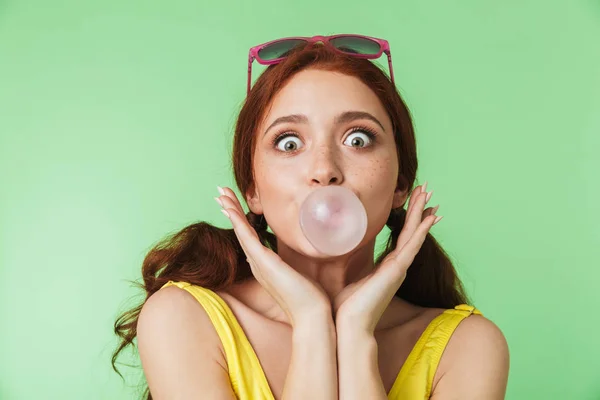 Redhead meisje poseren geïsoleerd over groene muur achtergrond met kauwgom. — Stockfoto