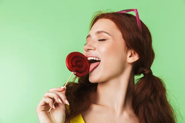 Hermosa joven pelirroja excitada posando aislada sobre fondo de pared verde con dulces . — Foto de Stock