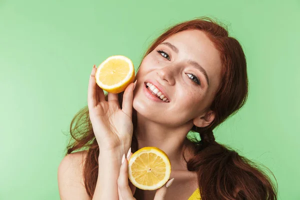 年轻的红头发女孩在绿墙背景上摆出孤立的姿势，用柑橘类维生素水果包裹着. — 图库照片