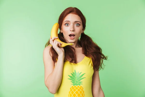 Shocked excited young redhead girl posing isolated over green wall background with bananas fruits. — Stock Photo, Image