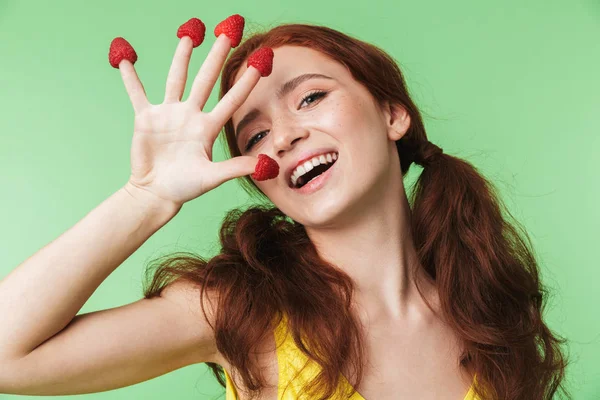 Hermosa chica pelirroja emocional joven posando aislado sobre fondo de pared verde con frambuesa . — Foto de Stock