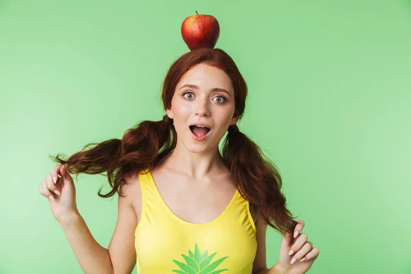 情绪化的年轻红发女孩在绿色墙壁背景与苹果构成孤立. — 图库照片