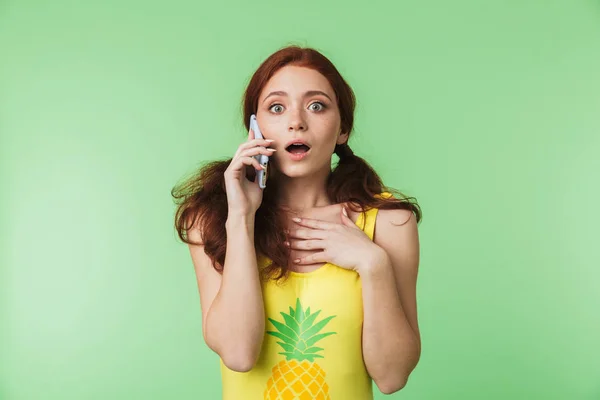 Krásná, šokovaná mladá rushlavka, která se izolovala na pozadí zelené zdi mluvící mobilním telefonem. — Stock fotografie