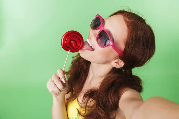 Hermosa joven pelirroja excitada posando aislada sobre fondo de pared verde con dulces . —  Fotos de Stock