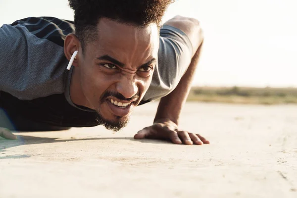 Bello giovane africano forte sportivo uomo ascolto musica con auricolari all'aperto fare esercizi . — Foto Stock