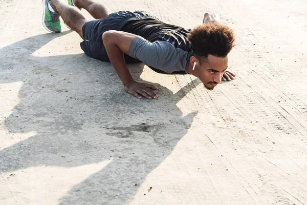 Bonito jovem africano forte homem de esportes ouvindo música com fones de ouvido ao ar livre fazer exercícios . — Fotografia de Stock