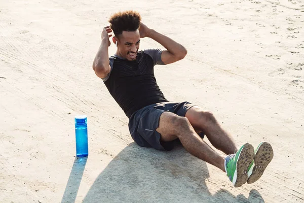 Bonito jovem africano forte homem de esportes ouvindo música com fones de ouvido ao ar livre fazer exercícios . — Fotografia de Stock