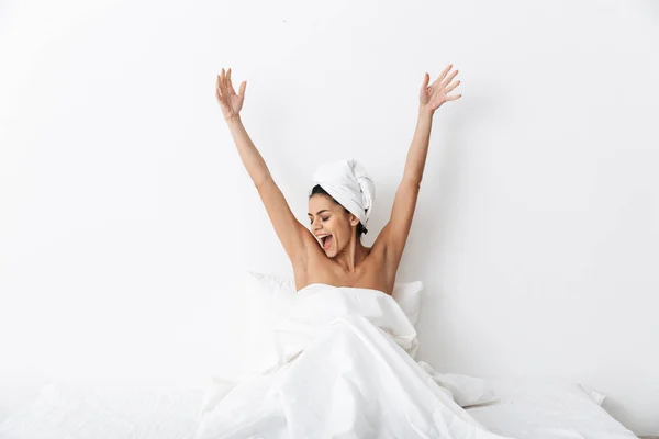 Mulher incrível bonita com toalha na cabeça encontra-se na cama sob cobertor isolado sobre fundo da parede branca . — Fotografia de Stock