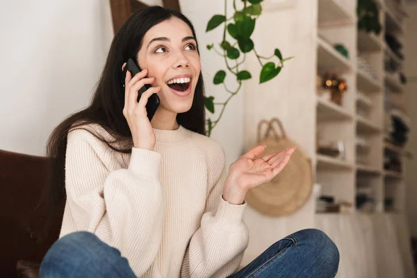 Foto einer jungen lächelnden Frau in den 20er Jahren, die im Sitzen mit dem Handy telefoniert — Stockfoto