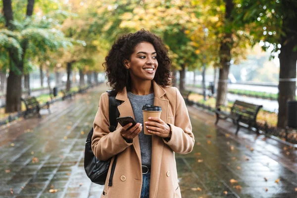 Hermosa mujer africana joven usando abrigo caminando al aire libre —  Fotos de Stock