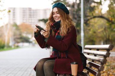 Palto ve bere giyen güzel genç kadın oturuyor