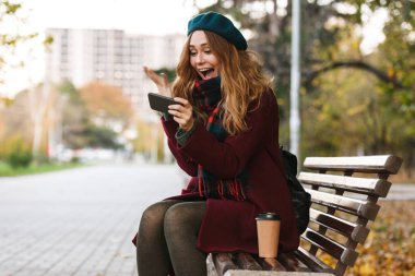 Palto ve bere giyen güzel genç kadın oturuyor