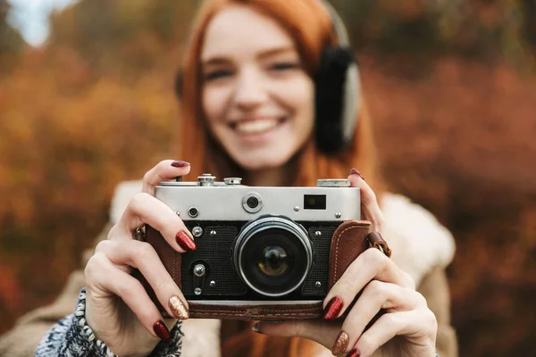 Lovely redheaded young girl listening to music, holding photo camera — Stock Photo, Image