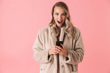 Akıllı telefonu tutan kürk manto giyen sürpriz sarışın kadın