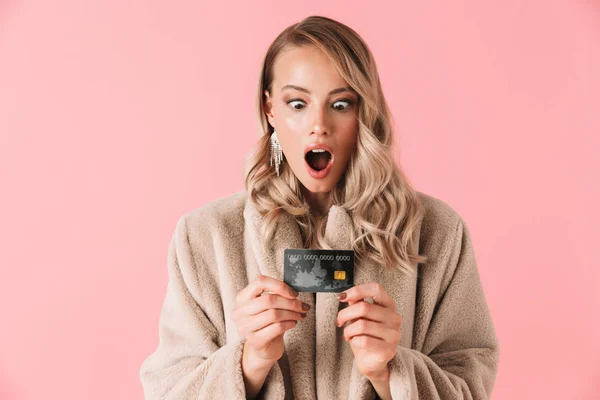 Mulher loira chocada vestindo em casaco de pele segurando cartão de crédito — Fotografia de Stock