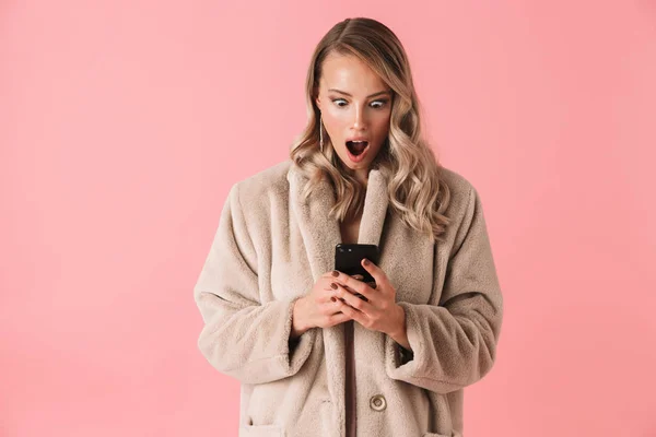 震惊的金发女郎穿着毛皮大衣使用智能手机 — 图库照片
