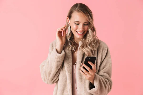 Mujer rubia sonriente vistiendo abrigo de piel escuchando música — Foto de Stock