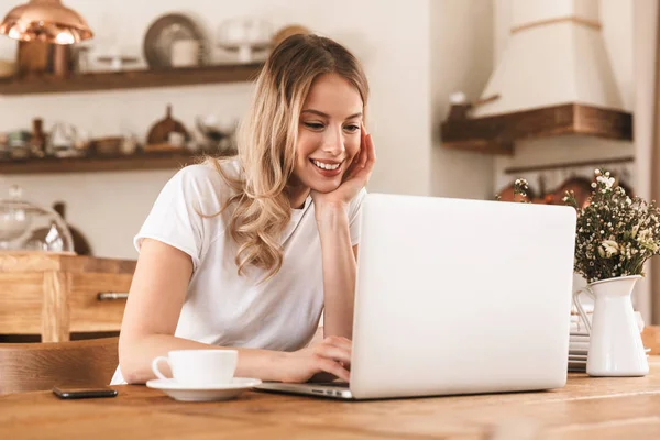 Portrait of satisfied blond woman working on laptop and drinking — Stock Photo, Image
