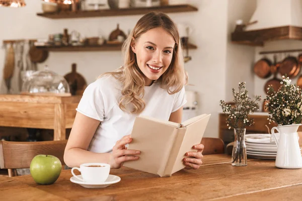 Портрет молодой блондинки, читающей книгу и пьющей кофе — стоковое фото