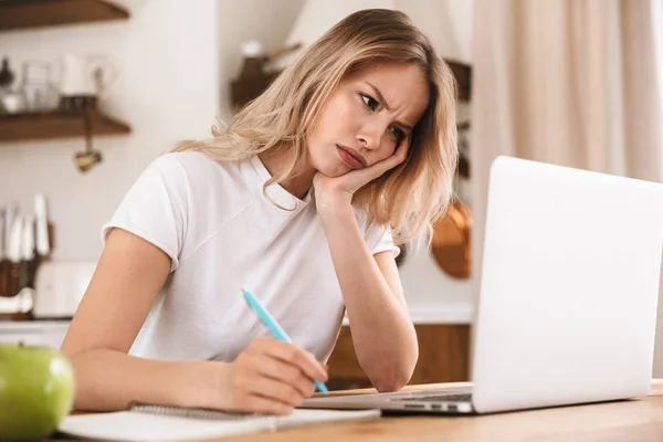 Bild av upprörd blond kvinna studerar på laptop och skriva ner n — Stockfoto