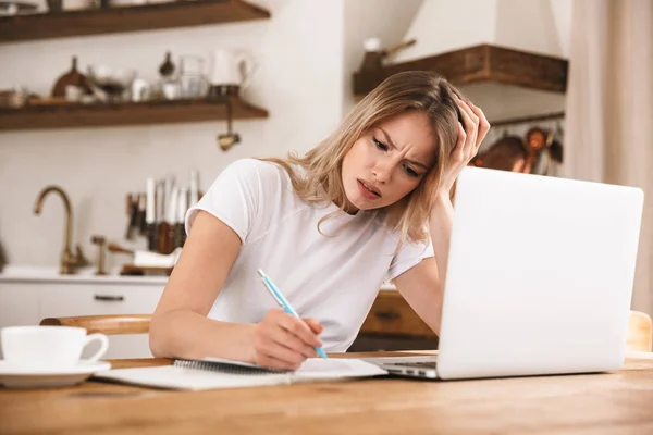 Obraz zaskoczony blond kobieta studiuje na laptopie i piśmie w dół — Zdjęcie stockowe