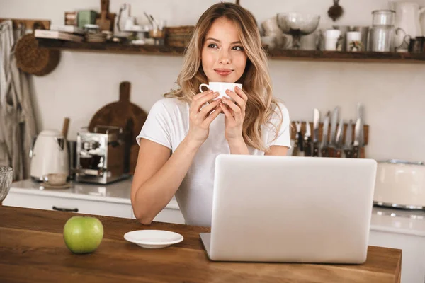 Bild av kaukasiska blonda kvinnan dricka te och använda laptop WHI — Stockfoto