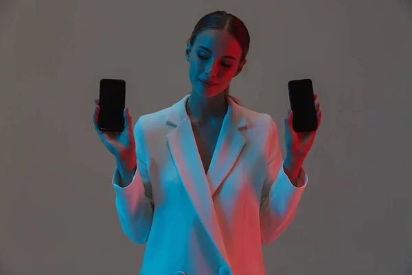Kép Vértes a divatos nő 20s gazdaságban két mobiltelefon — Stock Fotó