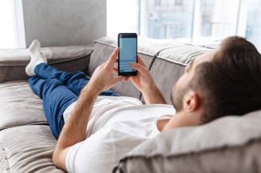 O yalan yaparken akıllı telefon tutarak ve kullanarak yakışıklı adam Fotoğrafı