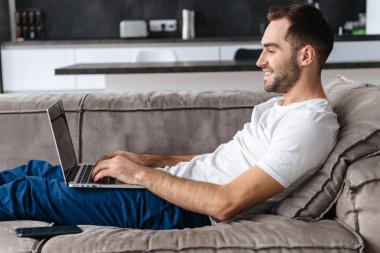 O yalan yaparken gümüş dizüstü bilgisayar tutarak ve kullanan genç adam Fotoğrafı