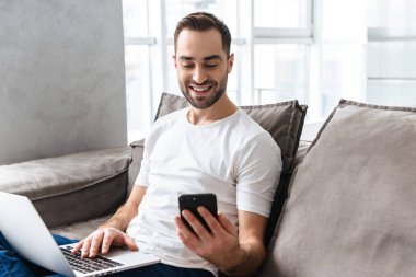 Akıllı telefon tutan ve gümüş lapto kullanarak memnun adam Fotoğrafı