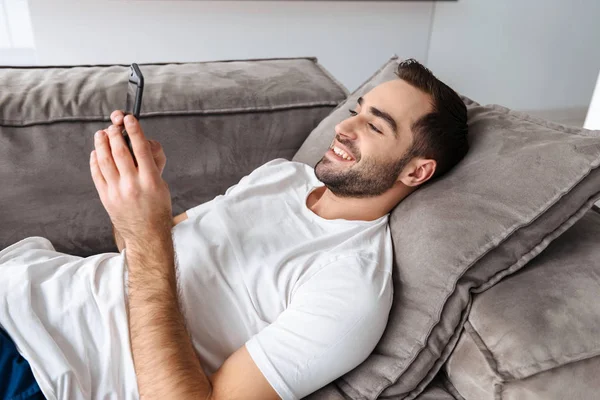 Foto av Happy Guy Holding och använda smartphone medan liggande på s — Stockfoto