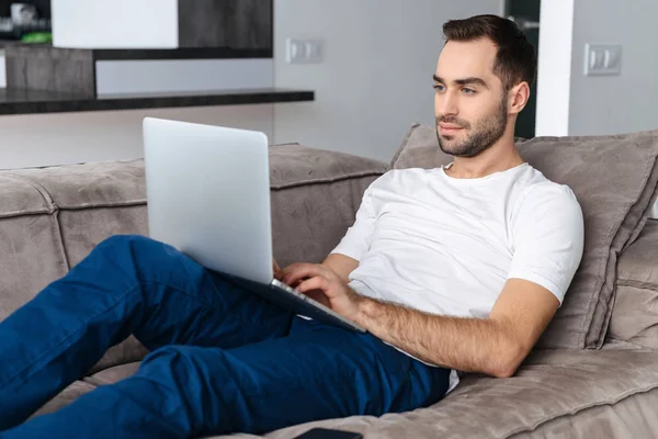 Foto di ragazzo europeo che tiene e utilizza il computer portatile d'argento mentre lyin — Foto Stock