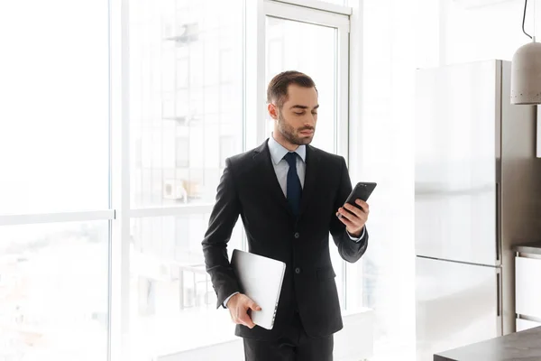 Beeld van knappe zakenman met behulp van mobiele telefoon tijdens het werken o — Stockfoto