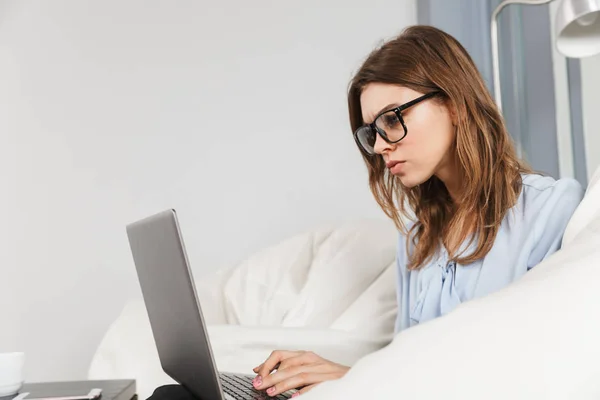 Concentrado hermosa joven bonita mujer en el hogar en el interior utilizando el ordenador portátil . — Foto de Stock