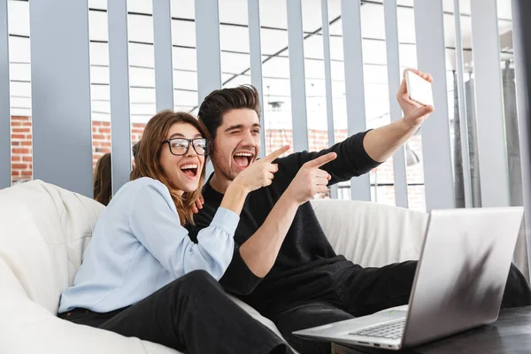 Felice giovane coppia amorevole a casa al chiuso utilizzando il computer portatile fare un selfie per telefono . — Foto Stock