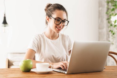 Dizüstü bilgisayar kullanarak kapalı oturan elma ile güzel genç öğrenci kız.