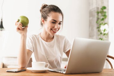 Dizüstü bilgisayar kullanarak kapalı oturan elma ile güzel genç öğrenci kız.