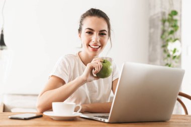 Dizüstü bilgisayar kullanarak kapalı oturan elma ile güzel genç öğrenci kız.