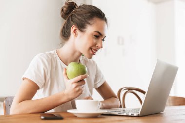 Dizüstü bilgisayar kullanarak kapalı oturan elma ile güzel genç öğrenci kız.