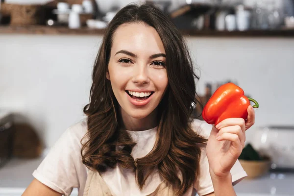 Vrolijk jong meisje dragen schort zittend in de keuken — Stockfoto