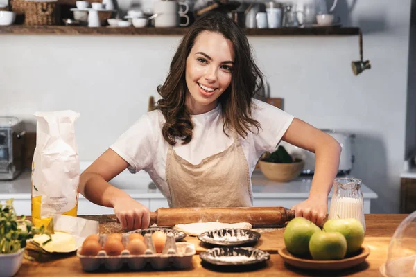 Vrolijke jonge vrouw draagt schort voorbereiding deeg — Stockfoto