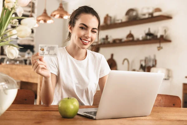 Hermosa chica estudiante joven con manzana en el interior usando computadora portátil con tarjeta de crédito . —  Fotos de Stock