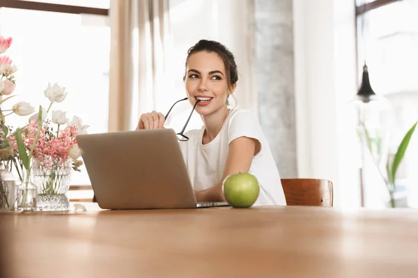 Vacker ung student tjej sitter inomhus med bärbar dator. — Stockfoto