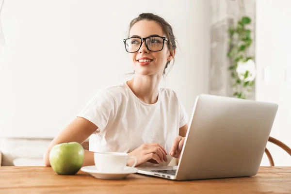 Hermosa chica estudiante joven con manzana sentado en el interior utilizando el ordenador portátil . — Foto de Stock