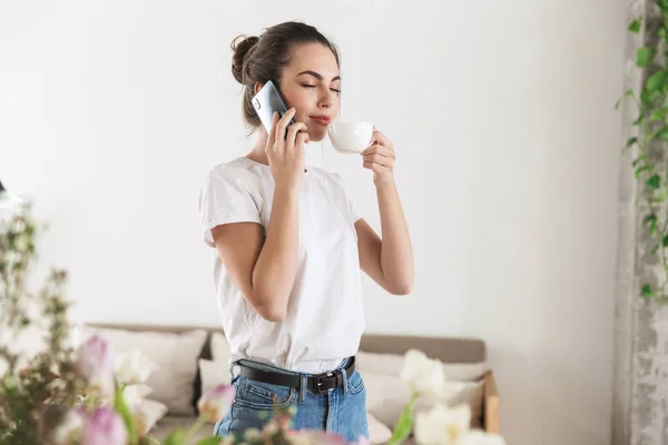 Estudante menina bebendo café posando dentro de casa falando por telefone celular . — Fotografia de Stock