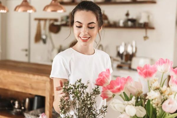 Jovem estudante feliz posando dentro de casa perto de flores . — Fotografia de Stock