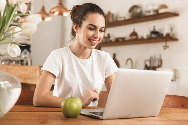 Hermosa chica estudiante joven con manzana en el interior utilizando el ordenador portátil . — Foto de Stock