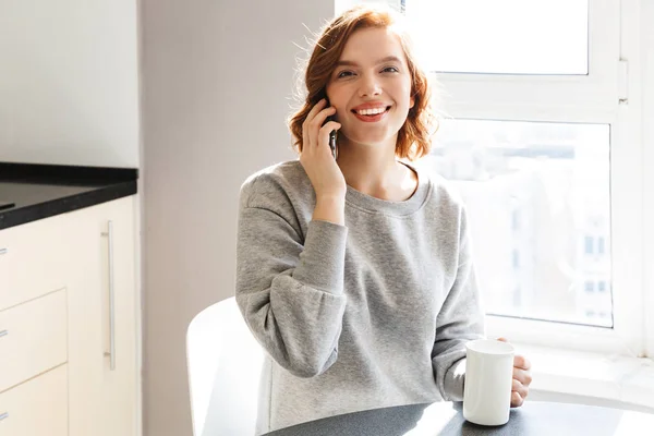 Smiling young woman drinking coffee while sitting at the table — Stock Photo, Image