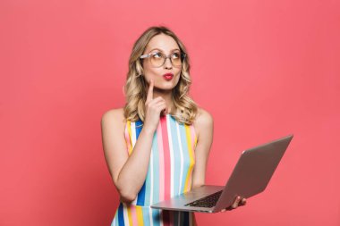 Güzel düşünen genç kadın dizüstü bilgisayar kullanarak kırmızı mercan arka plan üzerinde izole poz.
